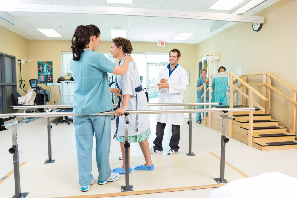 Mid adult female patient being assisted by physical therapist while doctor applauding